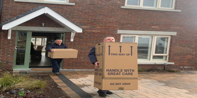 Frequently Asked Question Home Moves two men carrying boxes out of a house.
